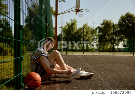 Sportsman tying shoelaces sitting on basketball court 106972090
