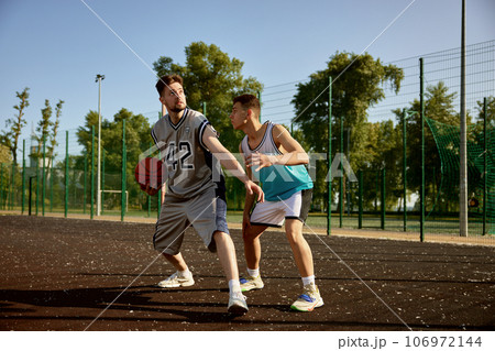 Active young men playing basketball on street court 106972144