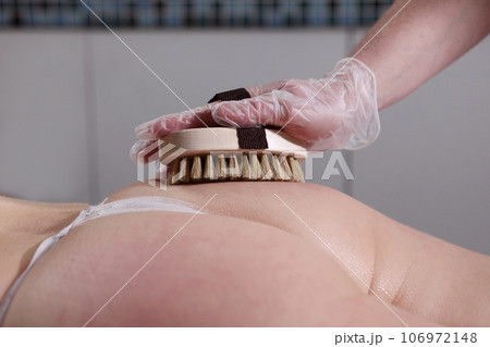 Body massage with brush with natural bristles.Body care. Exfoliation or peeling in beauty salon. 106972148