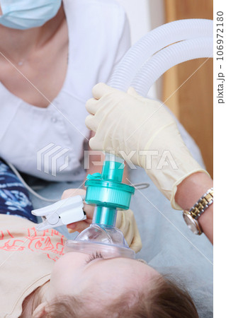 A little girl under general anesthesia. Breathing apparatus. Modern medicine and dentistry.Treatment of baby teeth. Vertical photo. 106972180
