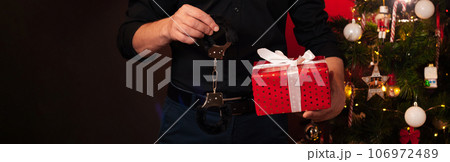 hands of a man with a gift box and BDSM handcuffs at the Christmas tree. Erotic gift for the new year for sexual games hands of a man with a gift box and BDSM handcuffs at the Christmas tree. Erotic gift for the new year for sexual games 106972489