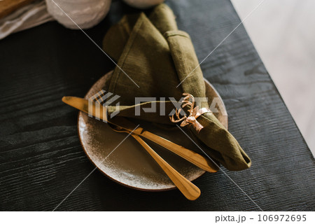 Christmas setting of the festive table. Dark green napkin and golden deer napkin ring and gold cutlery 106972695