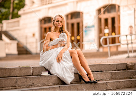 Woman city blanket. Morning in the big city. A blonde woman in a white blanket is enjoying in the city center. Photographed for social media Woman city blanket. Morning in the big city. A blonde woman in a white blanket is enjoying in the city center. Photographed for social media 106972824