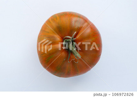 Large red, orange and green tomato with a tail, top view on a white background. Vegetables on a white background isolate. Large red, orange and green tomato with a tail, top view on a white background. Vegetables on a white background isolate. 106972826