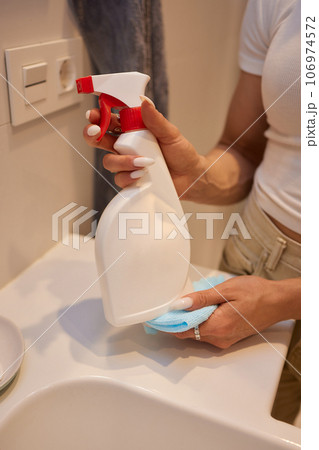 Cropped image of beautiful young woman using a duster and a detergent while cleaning sink and tap in bathroom. Cropped image of beautiful young woman using a duster and a detergent while cleaning sink and tap in bathroom. 106974572