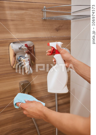 Cropped image of beautiful young woman using a duster and a detergent while cleaning sink and tap in bathroom. Cropped image of beautiful young woman using a duster and a detergent while cleaning sink and tap in bathroom. 106974573