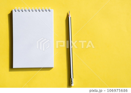 Open notepad and pencil or pen on yellow background. Composition of writing to-dos for the day. The notebook lies on a plain background with space for writing.  106975686