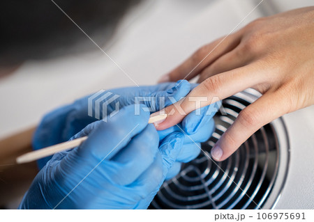 Nail care procedure in a beauty salon. Female hands and tools for manicure, process of performing manicure in beauty salon. Concept spa body care. Gloved hands of a skilled manicurist cutting cuticles 106975691