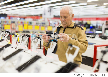 Elderly man buys a modern digital tablet in the showroom of the store 106976011
