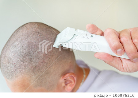 The hairdresser shaves the client's head with a white trimmer. Hairdressing salon, personal care. 106976216