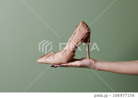 Female hand holds a brand new high heels shoes wrapped in rustic beige craft paper. Black Friday shopping concept. 106977156