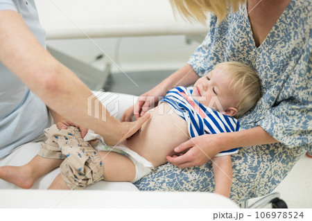 Infant baby boy child being examined by his pediatrician doctor during a standard medical checkup in presence and comfort of his mother. National public health and childs care care koncept 106978524