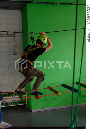 The boy actively and attentively passes the ropeway in the playroom. The boy actively and attentively passes the ropeway in the playroom. 106978526