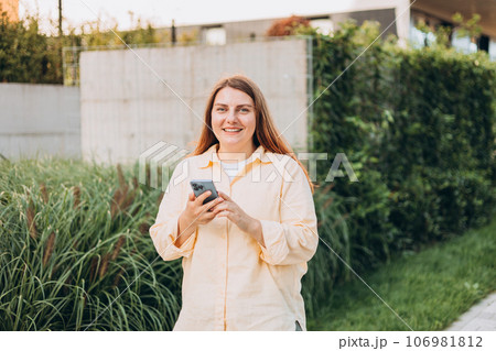 Young happy businesswoman smiling and using smart phone at the city. Beautiful woman on the way to the office searching information on the internet with smartphone. Business, education concept Young happy businesswoman smiling and using smart phone at the city. Beautiful woman on the way to the office searching information on the internet with smartphone. Business, education concept 106981812