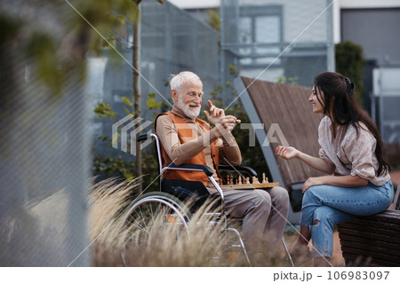 Senior man playing chess outdoors with his daughter. 106983097