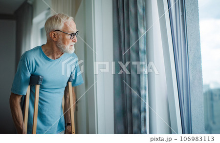 Senior man with crutches spending time alone in his apartment. 106983113
