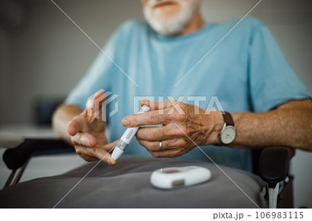 Diabetic senior man on wheelchair checking blood sugar level with fingerstick testing glucose meter. 106983115