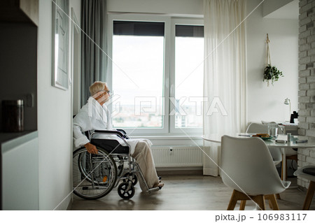 Senior man in a wheelchair spends time alone in his apartment. Senior man in a wheelchair spends time alone in his apartment. 106983117