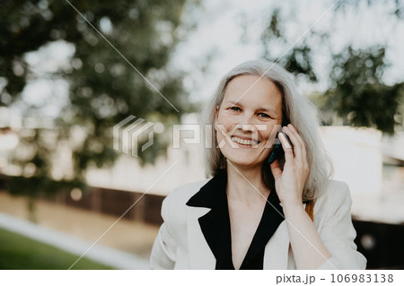 Portrait of beautiful female manager in middle age with gray hair walking through the city. Portrait of beautiful female manager in middle age with gray hair walking through the city. 106983138