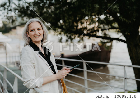 Portrait of beautiful female manager in middle age with gray hair walking through the city. 106983139