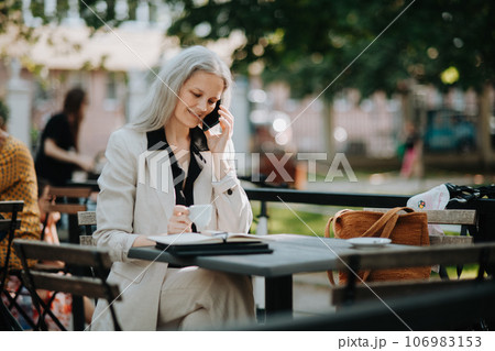 Portrait of beautiful female manager in middle age with gray hair making a phone call outdoors. Portrait of beautiful female manager in middle age with gray hair making a phone call outdoors. 106983153