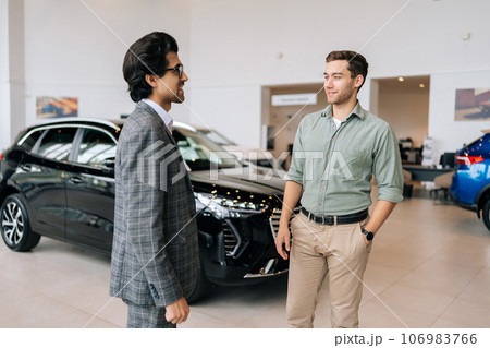 Friendly professional car dealer wearing business suit discussing new auto with cheerful male client man and woman in motor show. Concept of choosing and buying new auto at showroom. Friendly professional car dealer wearing business suit discussing new auto with cheerful male client man and woman in motor show. Concept of choosing and buying new auto at showroom. 106983766