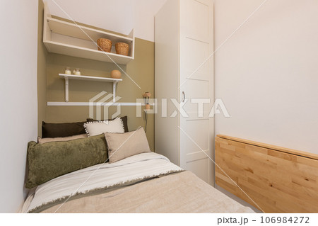 Bed on the background of shelves and narrow white wardrobe in a compact white bright five star hotel room for traveling a single person. Place for text Bed on the background of shelves and narrow white wardrobe in a compact white bright five star hotel room for traveling a single person. Place for text 106984272