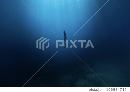 Freediver Swimming in Deep Sea With Sunrays. Young Man DIver Eploring Sea Life. Freediver Swimming in Deep Sea With Sunrays. Young Man DIver Eploring Sea Life. 106984713