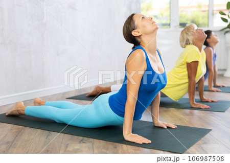 Middle-aged woman practicing cobra pose of yoga in fitness room 106987508