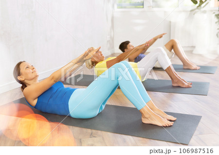 Group of people lying on floor doing yoga exercise boat pose. 106987516
