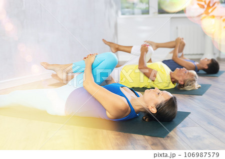 Mom, grandmother and teen grandson do preparatory stretching, lying on back and benting leg at knee Mom, grandmother and teen grandson do preparatory stretching, lying on back and benting leg at knee 106987579