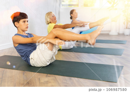 Preteen boy practicing boat pose of yoga in light fitness room 106987580