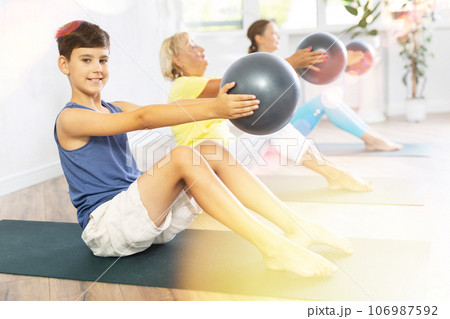 Preteen boy practicing seated fitness pose with softball in hands in training room 106987592