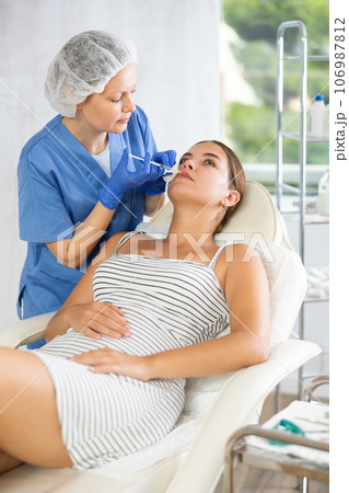 Adult woman cosmetologist makes injection in lips of patient 106987812