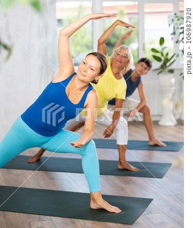 Middle-aged woman practicing side angle pose of yoga in light fitness room 106987920