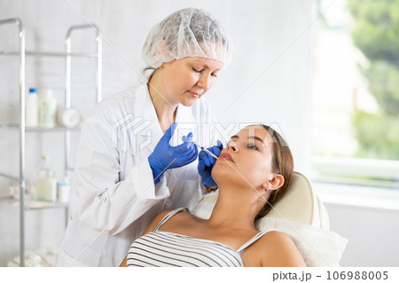 Doctor gives injection and performs procedure of lip augmentation of girl patient in clinic. 106988005