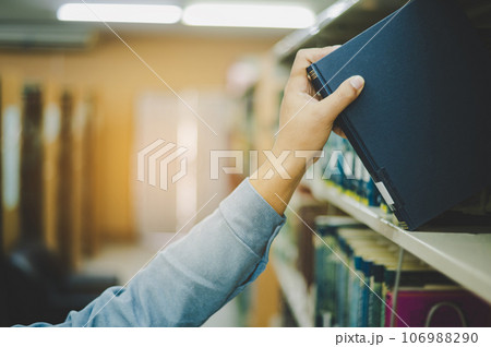 Close-up of hand picking up book on bookshelf in library to go to study.back to school concept 106988290