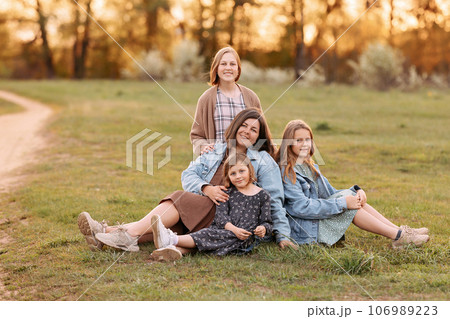 Happy mother and daughters sit hugging in a sunny field. 106989223