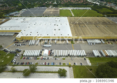 Top view of giant logistics center with many commercial trailer trucks unloading and uploading retail products for further shipment. Global economy concept Top view of giant logistics center with many commercial trailer trucks unloading and uploading retail products for further shipment. Global economy concept 106991346
