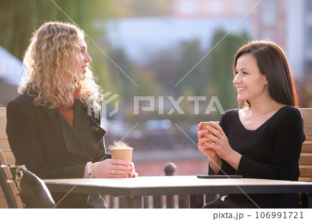 Portrait of two happy young women sitting at city street cafe Portrait of two happy young women sitting at city street cafe 106991721