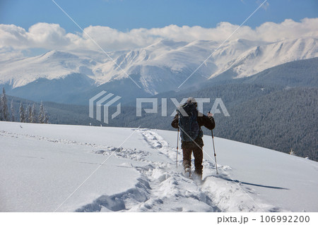 Man backpacker hiking snowy mountain hillside on cold winter day. 106992200