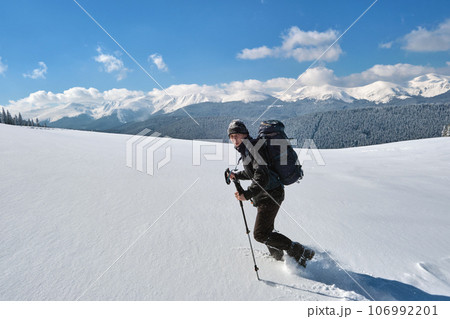 Man backpacker hiking snowy mountain hillside on cold winter day. 106992201