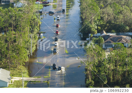 Hurricane flooded street with moving cars and surrounded with water houses in Florida residential area. Consequences of natural disaster 106992230
