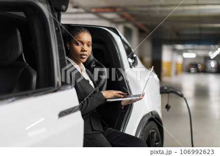 Professional operating computer in EV on charge in garage 106992623