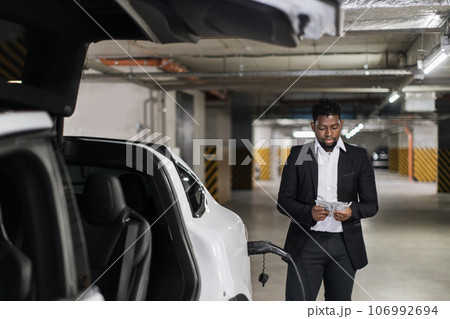 Adult in business suit thumbing through cash in EV parking Adult in business suit thumbing through cash in EV parking 106992694