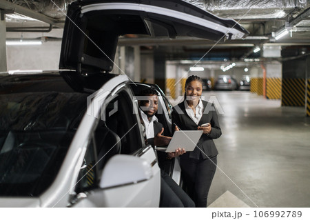 Partners operating laptop while sitting in EV in parking Partners operating laptop while sitting in EV in parking 106992789