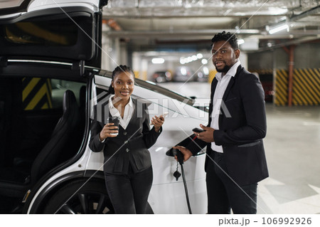 Coworkers with phones chatting near EV parking lot on break 106992926