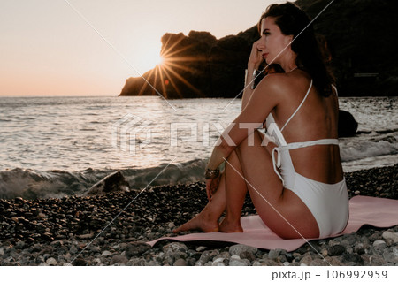 Woman sea yoga. Happy woman meditating in yoga pose on sunset beach, ocean and rock mountains. Motivation and inspirational fit and exercising. Healthy lifestyle outdoors in nature, fitness concept. Woman sea yoga. Happy woman meditating in yoga pose on sunset beach, ocean and rock mountains. Motivation and inspirational fit and exercising. Healthy lifestyle outdoors in nature, fitness concept. 106992959