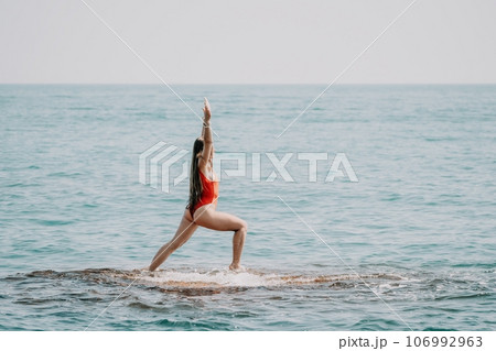 Woman sea yoga. Back view of free calm happy satisfied woman with long hair standing on top rock with yoga position against of sky by the sea. Healthy lifestyle outdoors in nature, fitness concept Woman sea yoga. Back view of free calm happy satisfied woman with long hair standing on top rock with yoga position against of sky by the sea. Healthy lifestyle outdoors in nature, fitness concept 106992963