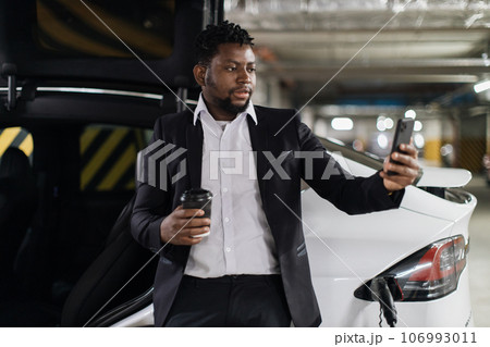 Worker with drink taking selfie near EV in basement parking 106993011